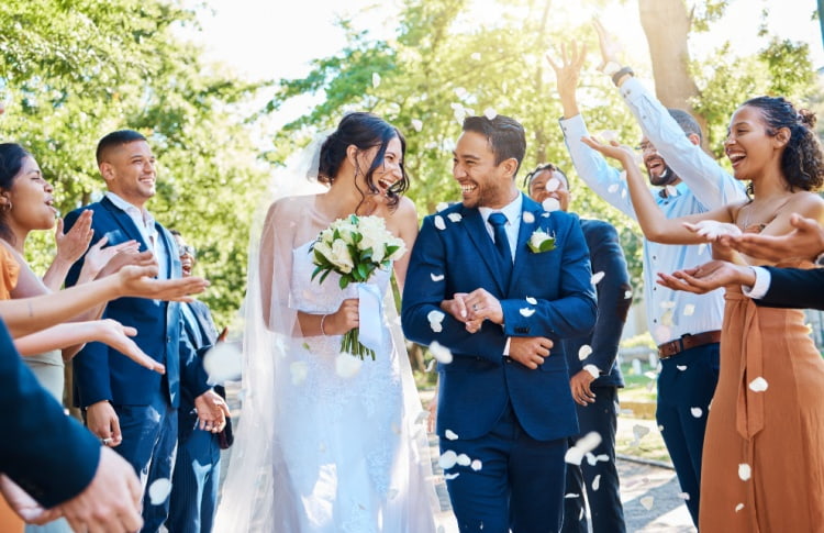 A bride and groom smile at each other while guests cheer